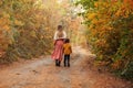 Mother and little son on walk in autumn forest, walking along path covered with yellow tree leaves Royalty Free Stock Photo