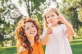 Mother looking at the camera while her daughter blowing soap bubbles in the park Royalty Free Stock Photo