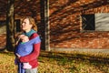 Mother lovingly carrying her newborn baby in a sling scarf during a sunset stroll in front of red brick building