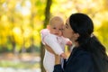 Mother kissing her baby in bright autumn park. Royalty Free Stock Photo