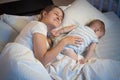 Young mother lying on bed at night next to her sleeping baby boy Royalty Free Stock Photo