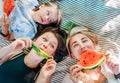 Mother lying with daughters lying on picnic blanket in city park during weekend sunny day, smiling, laughing at camera and eating Royalty Free Stock Photo