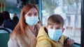 Mother and male child take precautions and wear medical mask while traveling on city bus