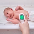 A mother measures the body temperature of a newborn baby with an infrared thermometer Royalty Free Stock Photo