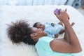 Mother and 1 month old baby newborn son lying on white bed and looking at mobile phone Royalty Free Stock Photo