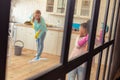 Mother mopping the floor and looking at her helpful daughter