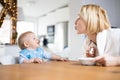 Mother motivating her baby boy infant child while spoon feeding him sitting in high chair at dinning table at home. Baby Royalty Free Stock Photo