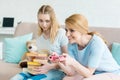 mother playing console game while her confused daughter sitting with stack of books Royalty Free Stock Photo