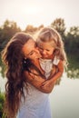 Mother playing and having fun with daughter by summer river at sunset. Woman holding kid and laughing. Family