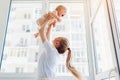 Mother playing with newborn baby son at home. Woman tossing kid up on balcony. Happy infant wearing diaper Royalty Free Stock Photo