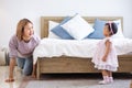 Mother is playing peek a boo or hide and seek with her little baby toddler in the bedroom while the girl is laughing in happiness