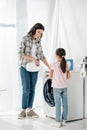 mother pouring liquid laundry detergent in washer wile daughter in pink t-shirt standing near