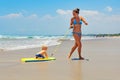 Mother pull baby son on surfing board by sea beach