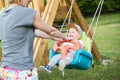 Mother pushing her infant baby boy child on a swing on playground outdoors.