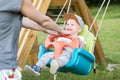 Mother pushing her infant baby boy child on a swing on playground outdoors.