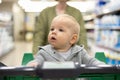 Mother pushing shopping cart with her infant baby boy child down department aisle in supermarket grocery store. Shopping Royalty Free Stock Photo