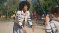 Mother pushing swing daughter playing on playground. Cute african girl swinging. Royalty Free Stock Photo