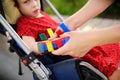 Mother puts orthosis on her daughter arms. Disabled girl sitting on a wheelchair. Child cerebral palsy