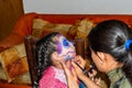 Young woman putting makeup of Catrina in a girl`s face