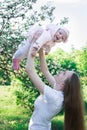 Mother raised daughter in her arms on nature background. Baby is flying and laughs. Vertical frame