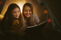 Mother reading a book to her daughter indoors before going to bed. Royalty Free Stock Photo