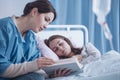 Mother reading a book to her sick, sleepy daughter in the clinic