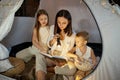 Mother reads a book of fairy tales for her children while sitting in a tent at night. Mom son and daughter reading a book Royalty Free Stock Photo