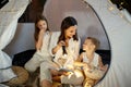 Mother reads a book of fairy tales for her children while sitting in a tent at night. Mom son and daughter reading a book with a Royalty Free Stock Photo