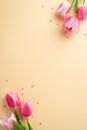 Top view vertical photo of bunches of pink tulips and heart shaped sprinkles on pastel beige background with copyspace