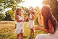 Mother`s day. Woman helps daughters to blow soap bubbles in summer park. Kids having fun playing outdoors