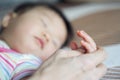 Mother`s hand holding of little young cute Asian baby sleeping on the bed. Close up view at baby fingers. Royalty Free Stock Photo