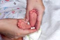 Mother`s hands hold the infant`s legs. The child`s foots are in mom`s palms