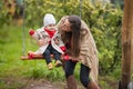 Mother shakes her baby on swing at the autumn park. Happy family spend time together Royalty Free Stock Photo