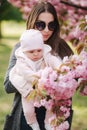 Mother show firs time to her daughter pink tree. Happy baby hold branch of sakura