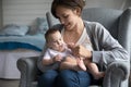 Mother sits on armchair in cozy bedroom with cute baby