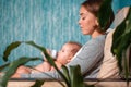 Mother is sitting in a chair and holding a baby in her arms, who is eating from a bottle. Side view. Concept of infant feeding and Royalty Free Stock Photo