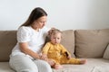 Mother sitting on couch with child and brushing baby hair with comb Royalty Free Stock Photo