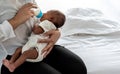 Mother Sitting on white bed, and feed milk from bottle milk to her 12-day-old baby black skin newborn son Royalty Free Stock Photo