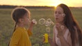 mother with small child blowing round soap bubbles sunset, happy family, cheerful kid and mom are playing with soap foam Royalty Free Stock Photo