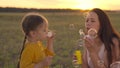 mother with small child blowing round soap bubbles sunset, happy family, cheerful kid and mom are playing with soap foam Royalty Free Stock Photo