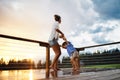 Mother with small daughter playing in rain on patio of wooden cabin, holiday in nature concept. Royalty Free Stock Photo