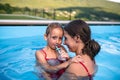 Mother with small daughter in swimming pool outdoors.