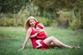 Mother and small dauther with blond hair and red dress sit on green grass