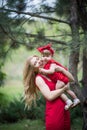 Mother and small dauther with blond hair and red dress stay on green grass