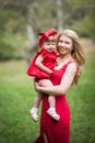 Mother and small dauther with blond hair and red dress stay on green grass