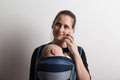 Mother with smartphone and baby sleeping in sling. Studio shot. Royalty Free Stock Photo