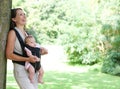 Mother smiling in park with baby in sling Royalty Free Stock Photo