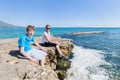 Mother and son as tourists sitting on rock near sea