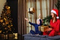 Mother and son on the bed in pajamas and a Santa hat with gifts on the background of a Christmas tree. The child throws the gift