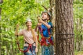 Mother and son climbing in extreme road trolley zipline in forest on carabiner safety link on tree to tree top rope